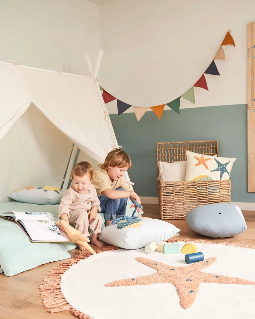 zwei Kinder auf einem Hausbett im Kinderzimmer mit Seesternteppich und diverse Kinderkissen