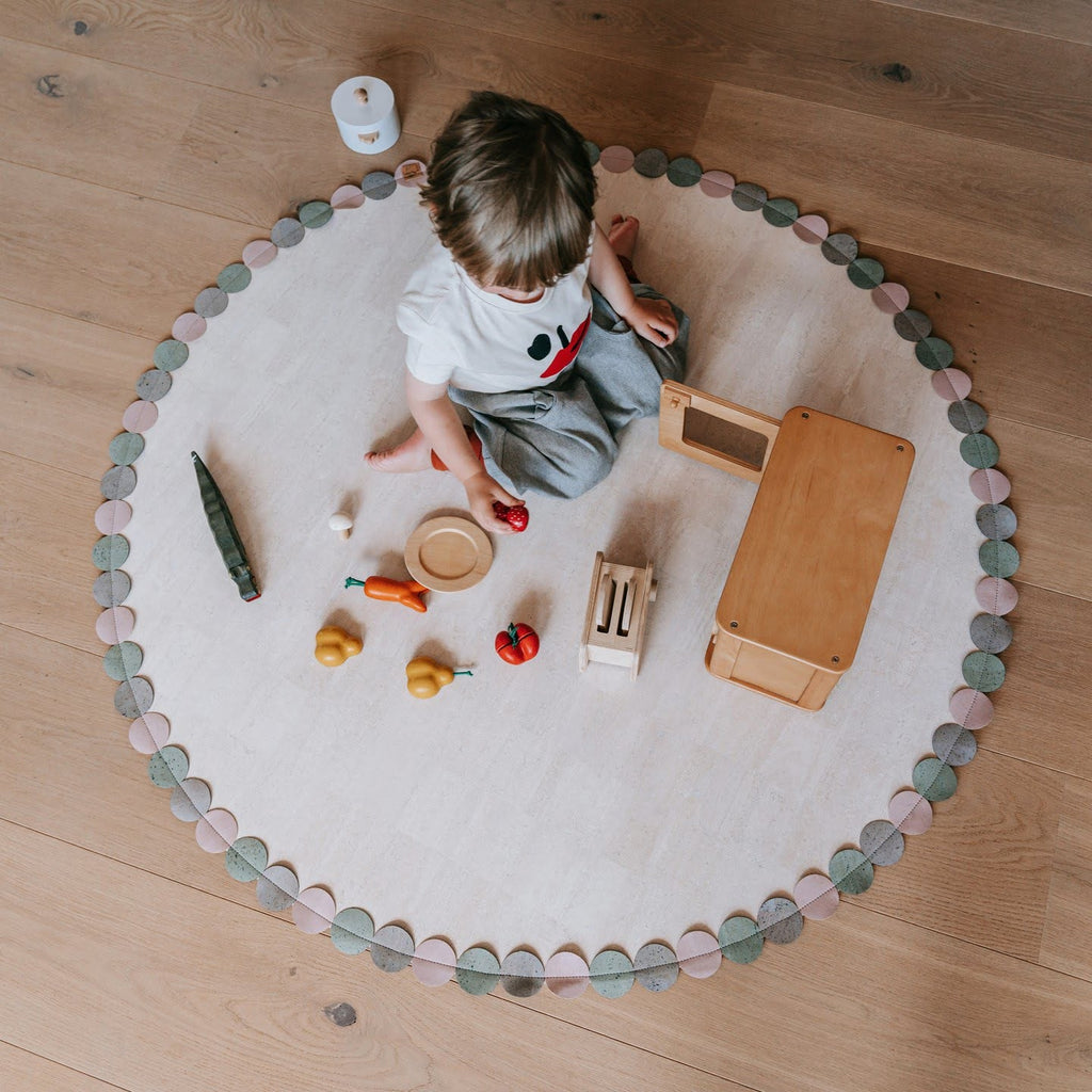 Kind auf runden Kork Teppich mit Holzspielsachen