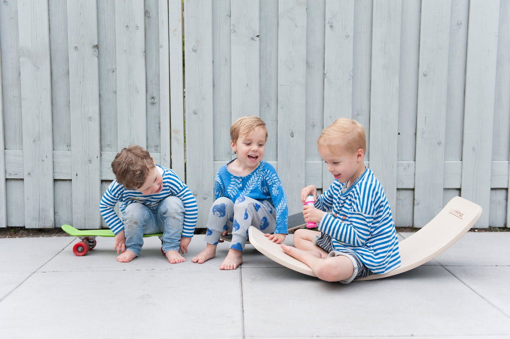 drei kinder spielen draußen auf dem Boden und sitzen auf Gleichgewichtsbrett aus Holz