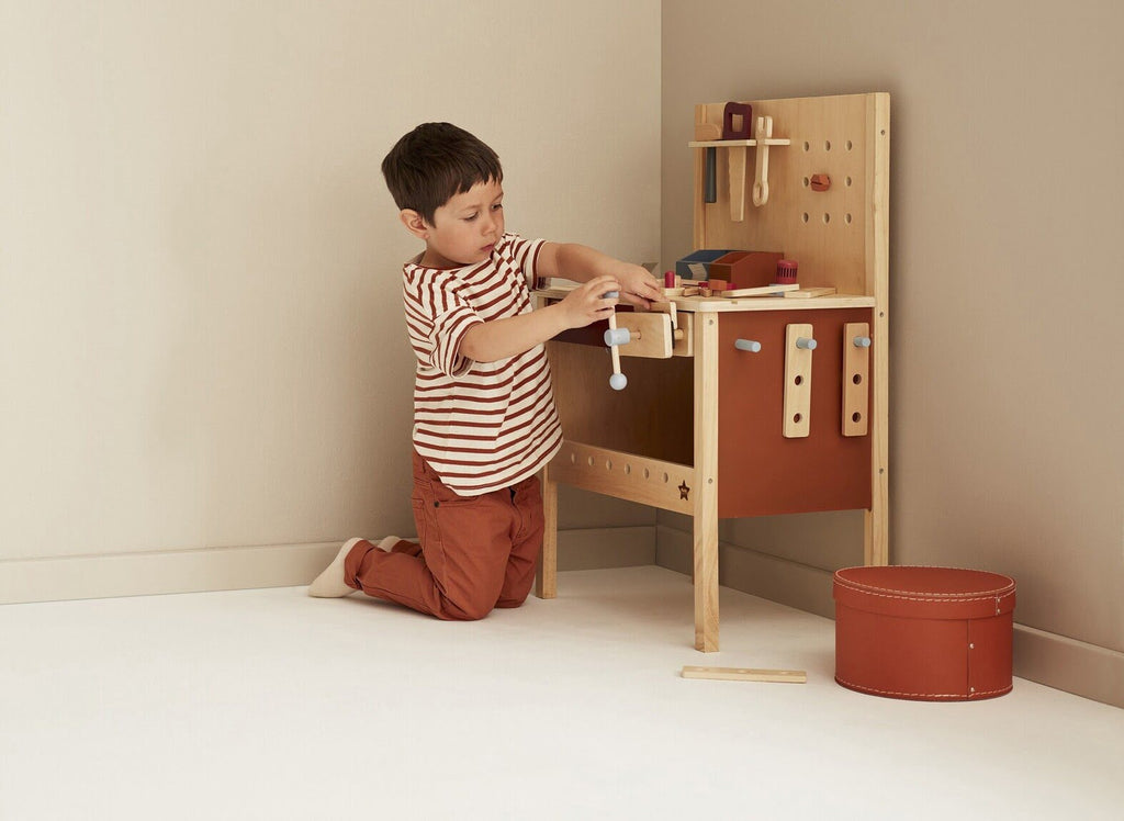 Kind spielt mit Werkzeugbank aus Holz mit viel Zubehör