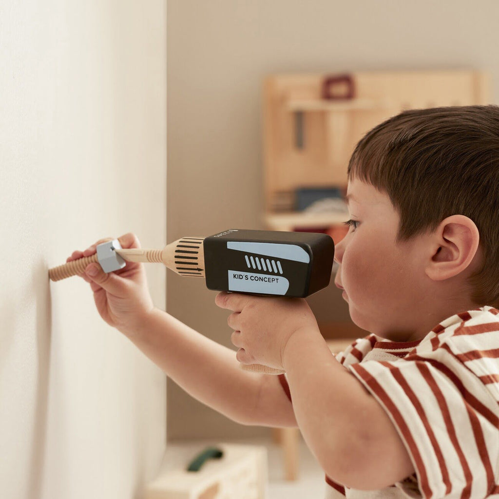Kind benutzt Akkuschrauber aus Holz mit Schraube an der Wand
