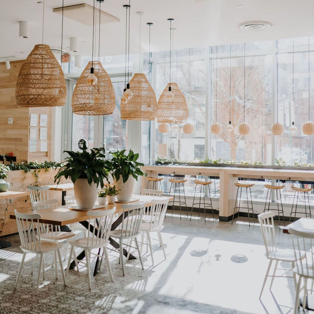 Restaurant mit weißen Stühlen und Tischen in Holz Naturnahe, Hocker am Fenster und hängen Rattenlampen und Pendelleuchten