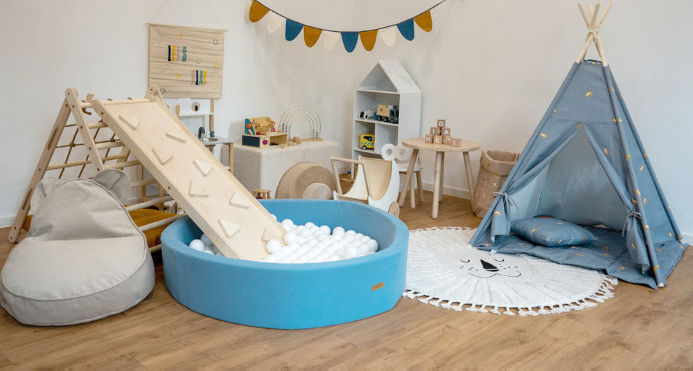 Spielzimmer modern beige weiß mit Bällebad in blau und Kletterdreieck, Kletterbrett und Tipi Zelt in blau und weitere Spielsachen aus Holz