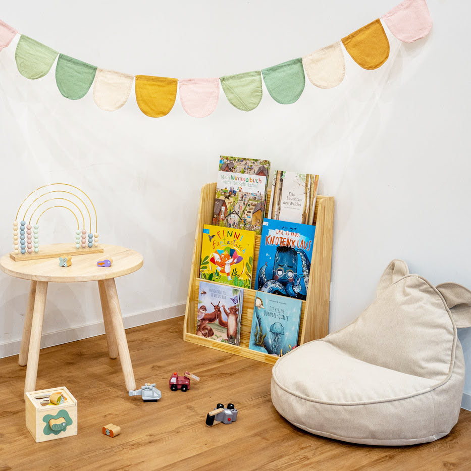 Bücherecke mit Sitzsack und kleinen Holzspielsachen auf rundem Kindertisch aus Holz mit Bücherregal aus Holz und Kinderbüchern