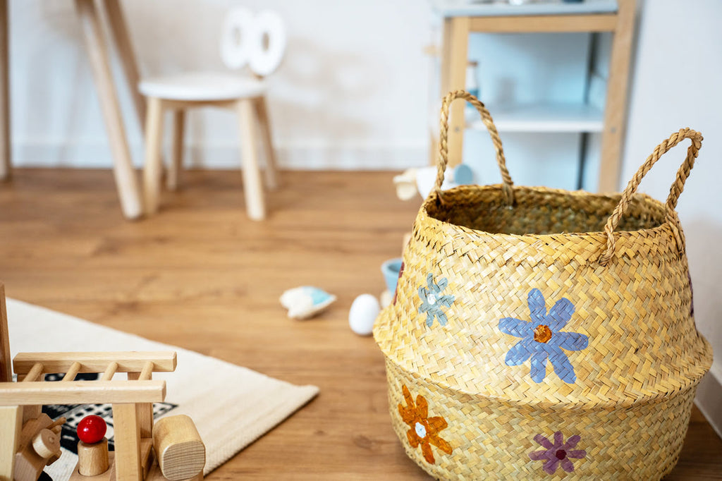 Spielzeugkorb aus Seegras mit Blumen und Spielsachen aus Holz im Hintergrund in Kinderecke