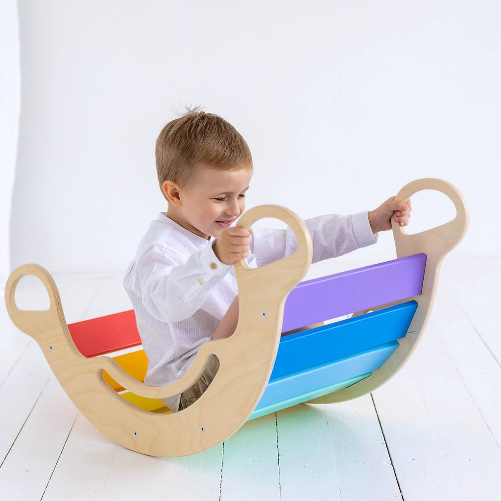 Kind schaukelt in der Balance Wippe Holz Regenbogenfarben
