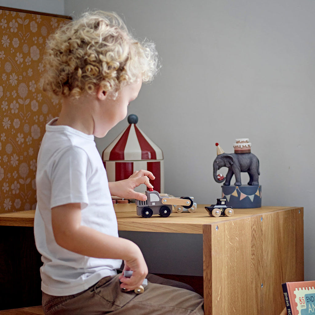 Kind spielt am Tisch mit Spielzeugauto Walze aus Holz in grau